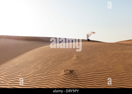 Teenager sitzen auf Wüste Dünen, Sand in die Luft werfen Stockfoto