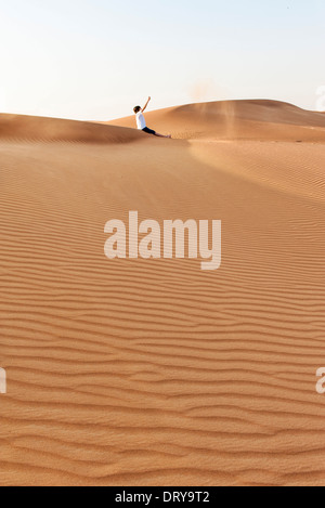 Teenager sitzen auf Wüste Dünen, Sand in die Luft werfen Stockfoto