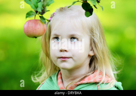 kleine Mädchen schaut nachdenklich auf den Apfel in einem Garten Stockfoto