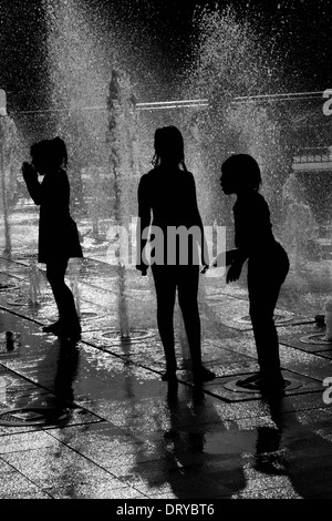 Silhouetten von Kindern beim Spielen im Wasser-Brunnen. Stockfoto