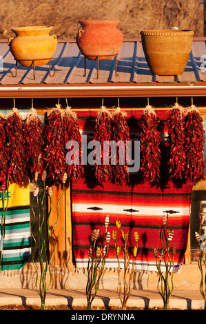 Getrocknete Paprika, Teppiche und Keramik Töpfe gegen eine Adobe-Struktur angezeigt und durch späte Nachmittagssonne beleuchtet. Stockfoto