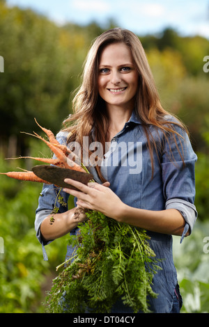 Junge Frau Gärtner hält eine Garbe von Möhren und eine Hacke in ihrem Garten, selektiven Fokus Stockfoto