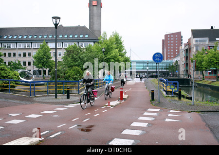 Radfahrer auf einem der Radwege in Houtens autofreien Innenstadt (im Hintergrund), eine niederländische Neustadt in der Nähe von Utrecht. Stockfoto