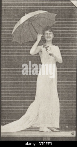 Eine Frau in einem drapierten Kleid öffnet einen Sonnenschirm und dreht sich um, gefangen in einem Moment anmutiger Bewegung. Stockfoto