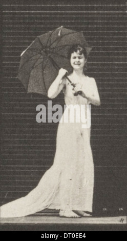 Eine Frau in einem drapierten Kleid öffnet einen Sonnenschirm und dreht sich um, um einen anmutigen Vintage-Moment festzuhalten. Stockfoto