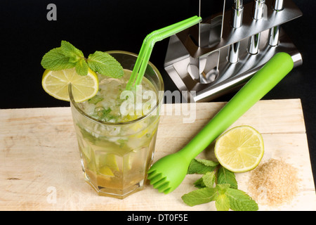 Mojito cocktail mit zwei Strohhalmen, Limettenscheibe und Minze Blätter, einige der Zutaten herum und ein cocktail Set hinter. Stockfoto