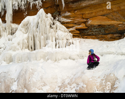 Eine Mädchen sitzt auf einer Eisbildung an den Apostel Insel Eishöhlen, Makwike Bay, nahe Bayfield, Wisconsin, an einem kalten Februartag. Stockfoto