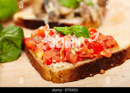 Nahaufnahme von Tomaten Bruschetta dekoriert mit Basilikum und Käse auf einem Holzbrett Stockfoto