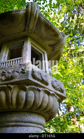 Kunstvoll geschnitzten japanische Steinlaterne zwischen den grünen Ahornbäumen im Garten. Stockfoto