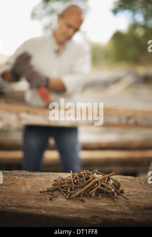 Ein Mann, der arbeitet in einem aufgearbeiteten Holz Hof Metalle aus Stück Holz A Haufen rostigen Metall Nägel entfernen Stockfoto