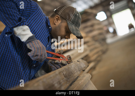 Ein Mann, der arbeitet in einem aufgearbeiteten Holz Hof mit einem Werkzeug, Metalle aus einem aufgearbeiteten Stück Holz Workshop zu entfernen Stockfoto