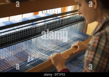 Eine Frau sitzend auf einem hölzernen Handwebstuhl eine handgewebte Wollstoff mit einem blau-weißen Muster erstellen Stockfoto
