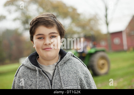 Ein Junge auf einem Bio-Bauernhof neben einem kleinen Traktor Stockfoto