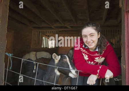 Ein Ziege Bauernhof Mädchen stützte sich auf die Barriere der Ziege Schuppen mit einer Gruppe von Ziegen hinter ihr Stockfoto
