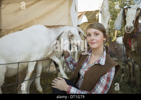 Ziegen in einem Kugelschreiber, beugte sich über die Zäune auf eine Farm A junge Frau kitzeln das Kinn eine weiße Ziege Stockfoto