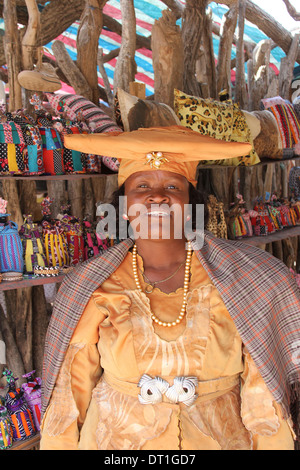 Herero-Frau in Tracht der deutschen Kolonialzeit und Kuhhorn Hut vor ihr Souvenir Puppen stand, Namibia.Africa Stockfoto