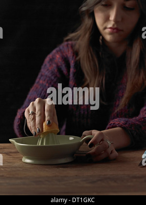 Eine Frau hält eine geschnittenen orange Hälfte und eine Orangenpresse verwenden, um den Saft auf einem Holztisch extrahieren Stockfoto