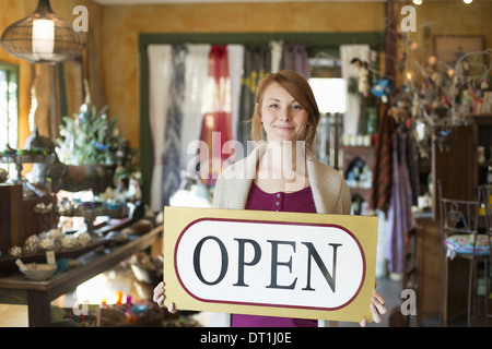 Eine Frau in einem Antiquitätengeschäft hält ein Schild "geöffnet" Displays waren alle um sie herum stehen Stockfoto