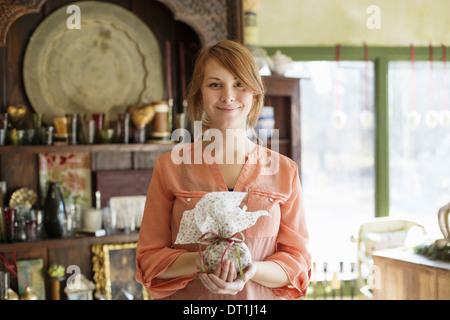 Eine junge Frau in einem Laden voller Antiquitäten hält eine gebundene Paket mit Schleife Stockfoto