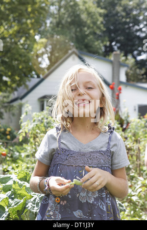 Ein junges Mädchen in einem blauen Stiefel und Schürze Kleid Lachen und halten grüne Bohnen, die sie aufgenommen hat Stockfoto