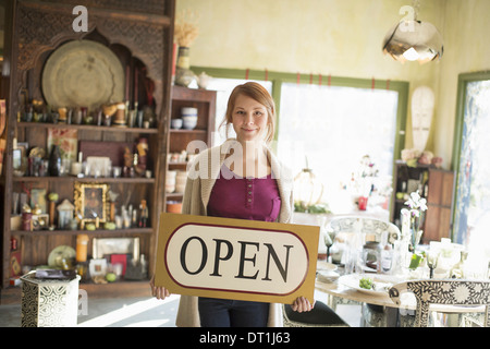 Eine Frau in einem Antiquitätengeschäft hält ein Schild "geöffnet" Displays waren alle um sie herum stehen Stockfoto