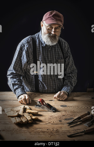 Ein Mann arbeitet in einer aufgearbeiteten Holzplatz Werkstatt Werkzeuge halten und arbeiten an einem verknotet und unebene Stück Holz Stockfoto