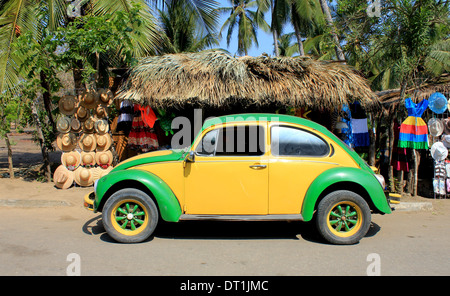 Gelb und grün VW Käfer Bug in der Nähe von Strand, Ventanilla, Oaxaca, Mexiko mit Palmendach Markt stehen hinter dem Verkauf von Hüten und Kleidung Stockfoto