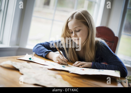 Eine Familie zu Hause ein junges Mädchen sitzt an einem Tisch auf einem großen Blatt Papier mit einem Bleistift zeichnen Stockfoto