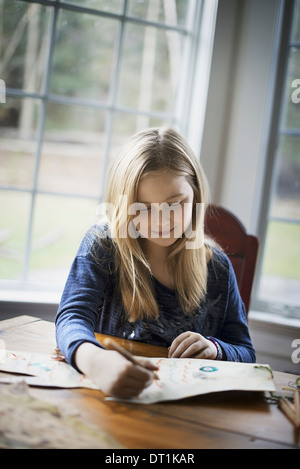 Eine Familie zu Hause ein junges Mädchen sitzt an einem Tisch auf einem großen Blatt Papier mit einem Bleistift zeichnen Stockfoto