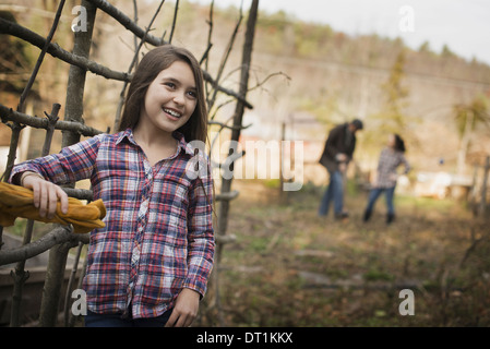 Ein junges Mädchen, stützte sich auf einen Zaun und zwei Personen im Hintergrund einen Bio-Bauernhof Stockfoto