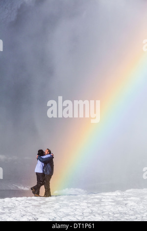 Regenbogen über Skogafoss Wasserfall im Winter Island Paar genießt die Nähe zu den Wasserfall mit einem schönen Regenbogen. Stockfoto