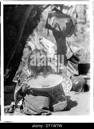 Eine Havasupai-Indianerin, Chick-a-Pan-a-gie's Frau, wird 1898 in einem Korb geparst. Das Bild zeigt traditionelle Methoden der Zubereitung von Speisen des Havasupai-Stammes. Stockfoto