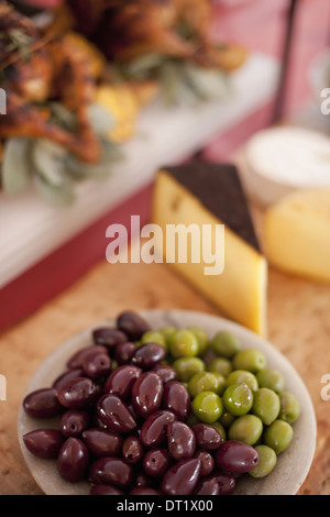 Ein Buffet-Tisch ausgelegt für eine Partei Bio-Lebensmittel A Board Käseauswahl und einen Teller mit grünen und schwarzen Oliven Stockfoto