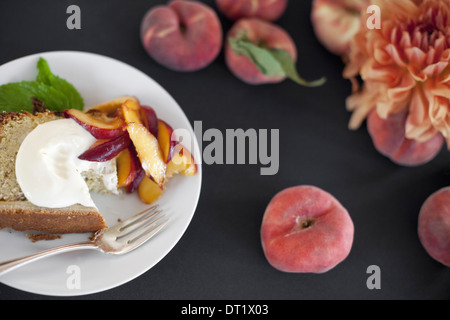 Eine Tabelle gesehen von oben Bio-Obst Pfirsiche und Blumen einen Teller mit frischem Obst Kuchen und Creme Fraiche eine Gabel Dessert Stockfoto