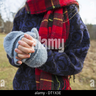 Eine Frau in einen Tartan-Schal und gestrickte wollene Handschuhe halten ihre Hände warm in der kalten Jahreszeit Stockfoto