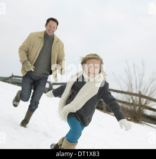 Ein Mann jagt ein junges Mädchen im Schnee Bauernhof im winter Stockfoto