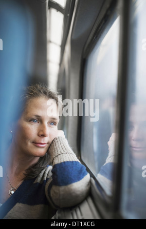 Eine Frau sitzt an einem Fensterplatz in einem Zug Wagen ihren Kopf auf ihre Hand ruht Blick in die Ferne Stockfoto