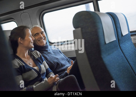 Zwei Menschen sitzen in einem Eisenbahnwagon lächelnd, wobei eine Zugfahrt Stockfoto