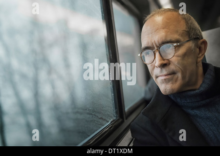 Ein reifer Mann sitzen in einem Fensterplatz auf einer Zugfahrt in die Ferne schauen Stockfoto