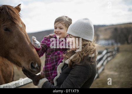 Eine Frau und Kind klopfte ein Pferd in einer Koppel auf einem Bauernhof Stockfoto