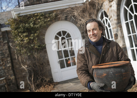 Frühling, einen Mann mit einem großen Terrakotta-Topf über einen Hof zu Pflanzen Stockfoto