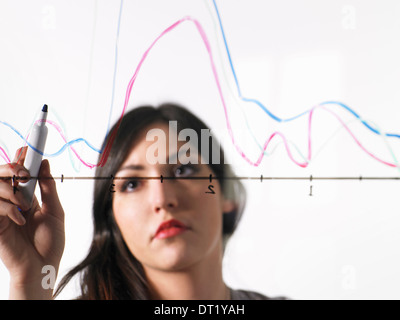 Eine junge Frau, die farbige Grafik Linien über eine Grafik Illustration auf einen durchsichtigen Oberfläche zeichnen Stockfoto