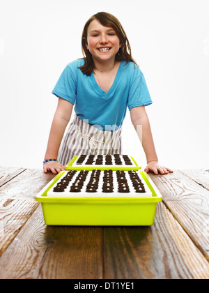 Ein junges Mädchen, stützte sich auf eine Tabelle mit zwei Tablett mit frisch gepflanzten Samen ruht auf dunklen organischen Böden