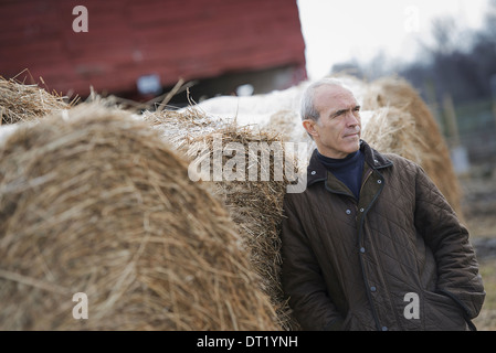 Ein Bio-Bauernhof im Winter ein Mann stehend neben großen Heuballen Stockfoto