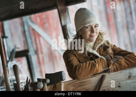 Eine Frau in einem Schaffell Mantel eine Reihe von Handwerkzeugen auf einem Pfosten hängen Stockfoto