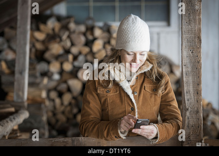 Ein Bio-Bauernhof im Bundesstaat New York im Winter A Frau in Schaffell Fell und Wolle Hut mit einem Handy Stockfoto