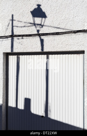 Schatten der Lampost und Pol mit Kabel am Garagentor und Wand. Stockfoto
