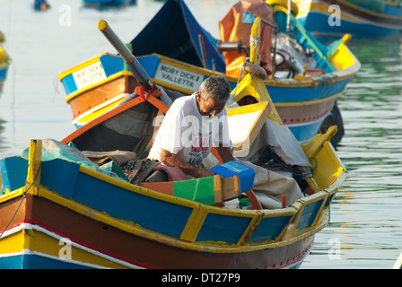 Maltesische Fischer bei der Arbeit in seinem Luzzu oder traditionellen Boot in den Hafen von Marsaxlokk Stockfoto