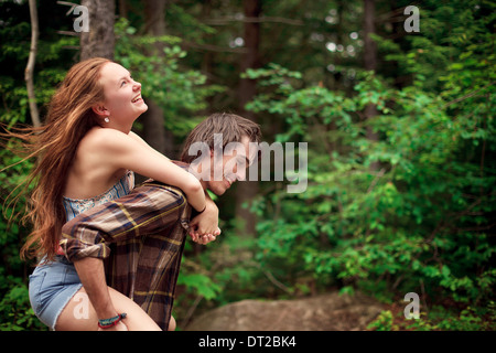 Junger Mann und junge Frau Huckepack Fahrt durch Wald Stockfoto