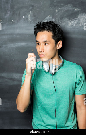 Schöner asiatischer Mann tragen Kopfhörer, singen und tanzen zur Musik. Steht man vor einer Tafel. Stockfoto